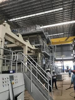 Equipo con casco junto a escaleras de máquina industrial en nave