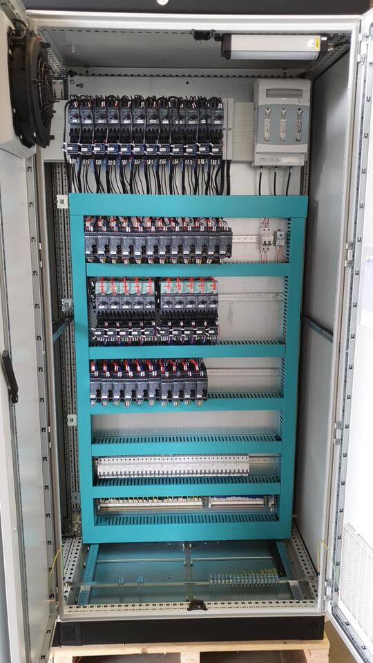 Panel abierto sobre palé con seccionador fusible, disyuntores y ventilador en la puerta