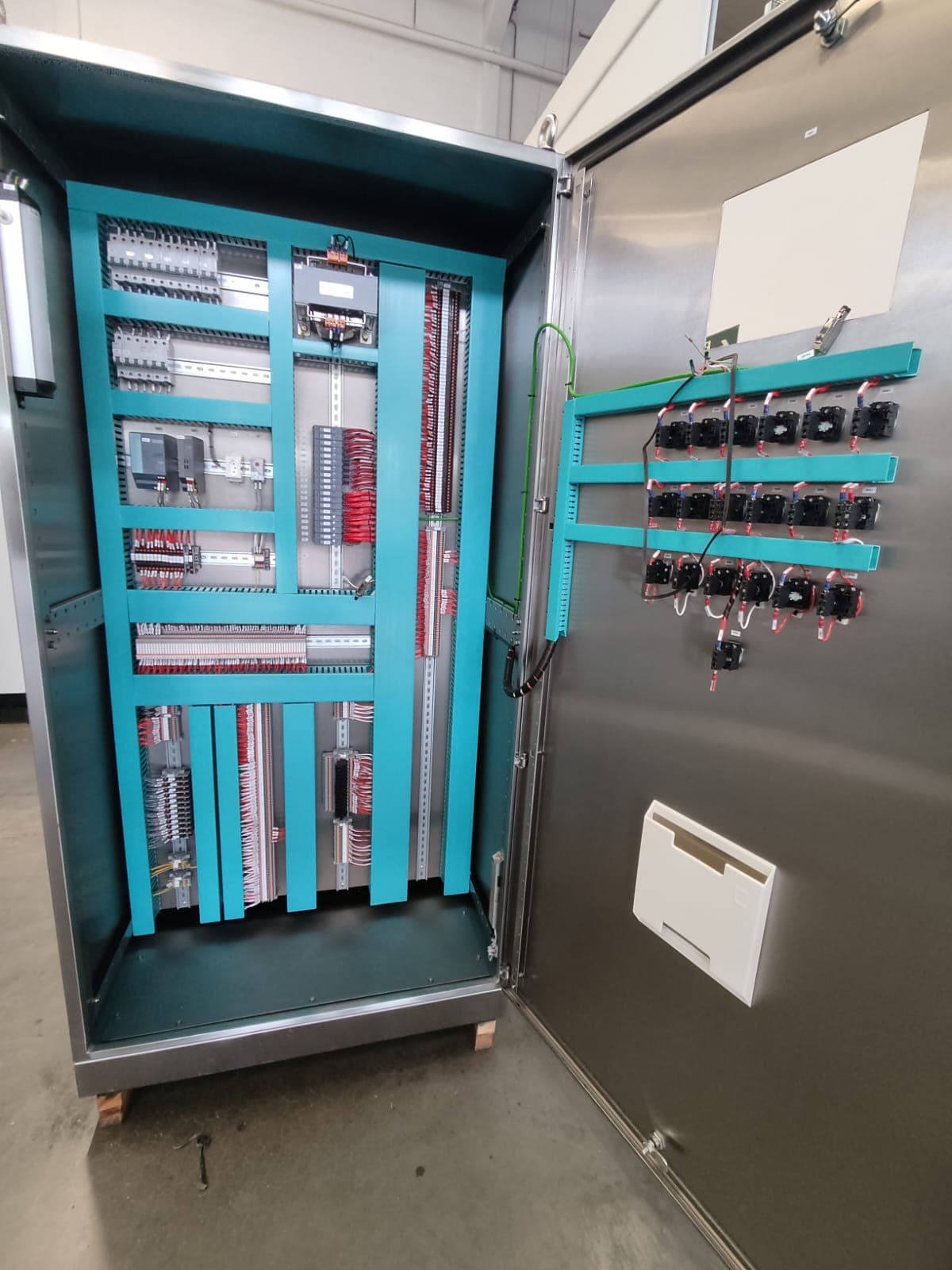 Panel de inox abierto con interior turquesa, bornes y componentes en la puerta